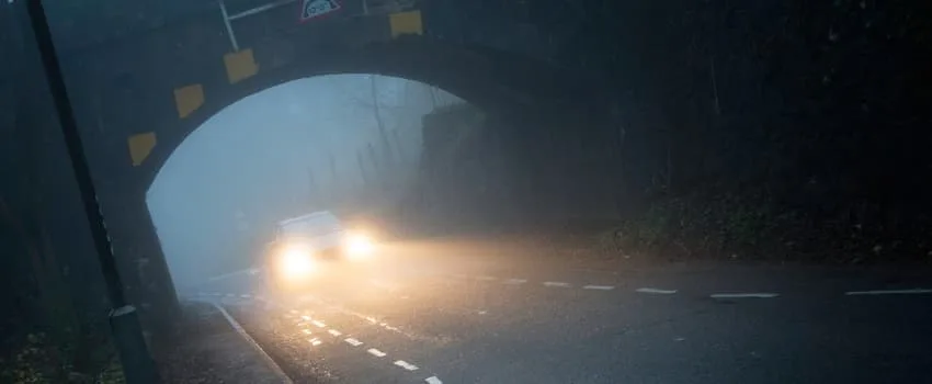 Car or vehicle on the road at night in foggy conditions. Angled dramatic shot showing fog and danger. Passing under arched bridge