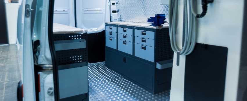 Interior of a custom mobile workshop van fitted with secure storage drawers, shelving, a workbench and equipment, designed for engineers and field service professionals.