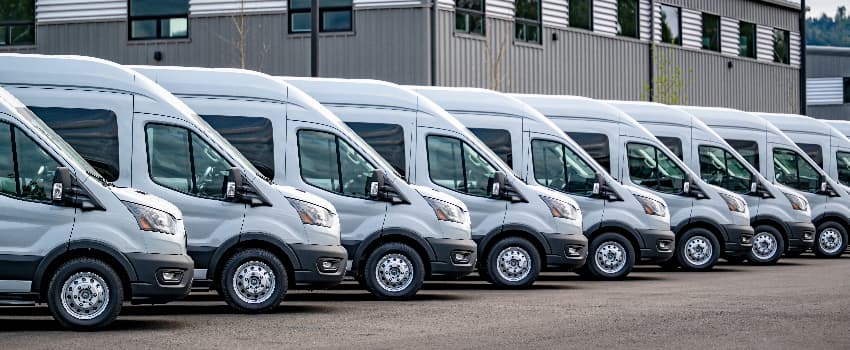 A fleet of white commercial vans parked in a row outside an industrial building.